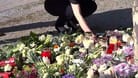 Bad Oeynhausen: Eine Frau stellt eine Kerze neben Blumen, während Menschen nach einem tödlichen Angriff im Kurpark trauern.