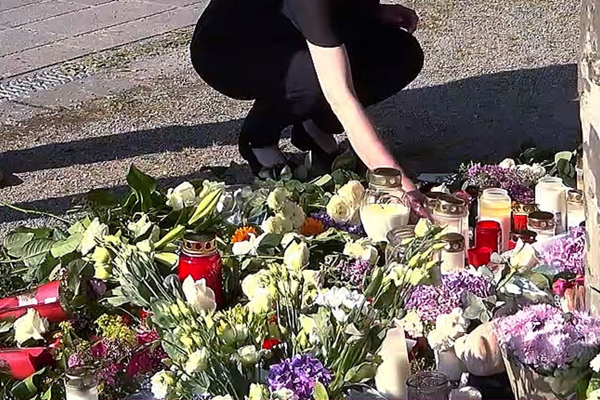 Bad Oeynhausen: Eine Frau stellt eine Kerze neben Blumen, während Menschen nach einem tödlichen Angriff im Kurpark trauern.