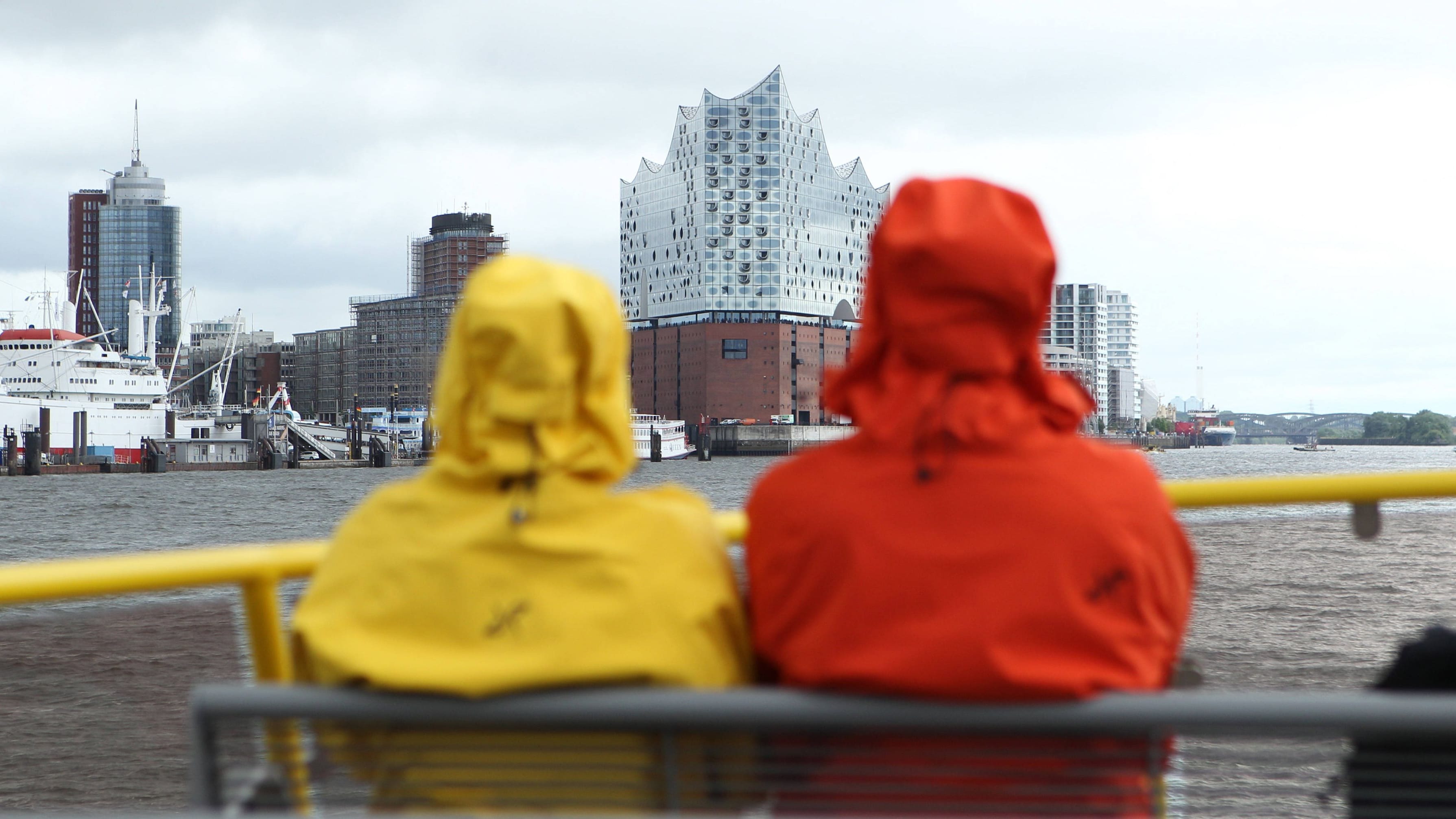 Eine Frau und ein Mann sind mit Regenjacken an Deck einer HADAG-Fähre (Symbolfoto): Das Wetter in Hamburg und Schleswig-Holstein bleibt durchwachsen.