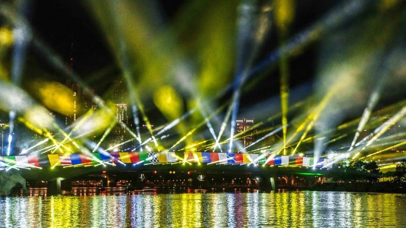 Eine audiovisuelle Lichtinszenierung auf der Flößerbrücke stimmt die Besucher auf das sportliche Großereignis ein: Ab Freitag eröffnet auch die Fan Zone in Frankfurt.