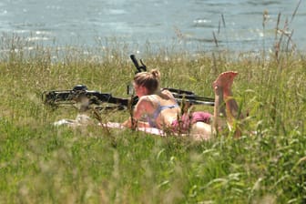 Eine junge Frau liegt am Rhein (Symbolbild): In dieser Woche wird es endlich sommerlich warm.