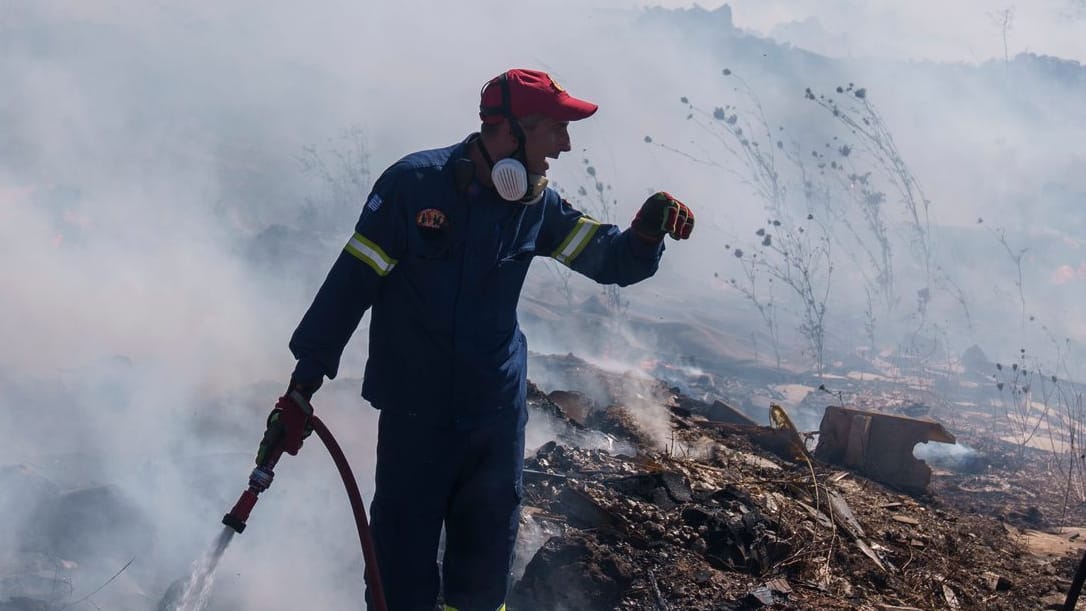 Feuerwehrleute versuchen, ein Feuer zu löschen, während ein Löschhubschrauber Wasser im Vorort Koropi im Osten von Athen abwirft.