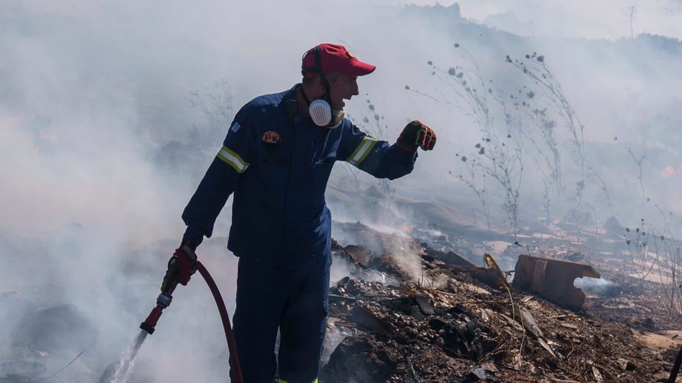 Feuerwehrleute versuchen, ein Feuer zu löschen, während ein Löschhubschrauber Wasser im Vorort Koropi im Osten von Athen abwirft.