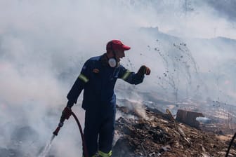 Feuerwehrleute versuchen, ein Feuer zu löschen, während ein Löschhubschrauber Wasser im Vorort Koropi im Osten von Athen abwirft.