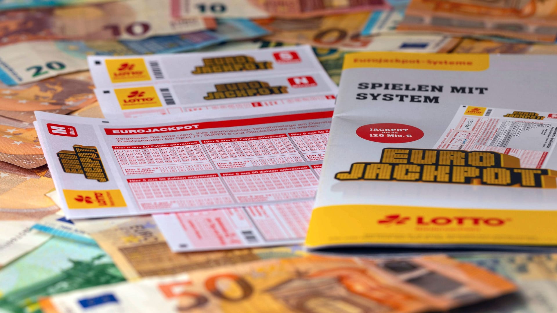 Geldscheine liegen neben einem Eurojackpot-Spielschein (Symbolfoto): In Bayern haben am Dienstag zwei Spieler große Summen gewonnen.