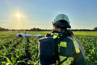 Ein Feuerwehrmann auf einem Acker in Hünxe: Das Flugzeug vor ihm landete kopfüber auf dem Feld.