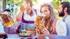 Woman in Tracht looking into camera while drinking a mass of beer