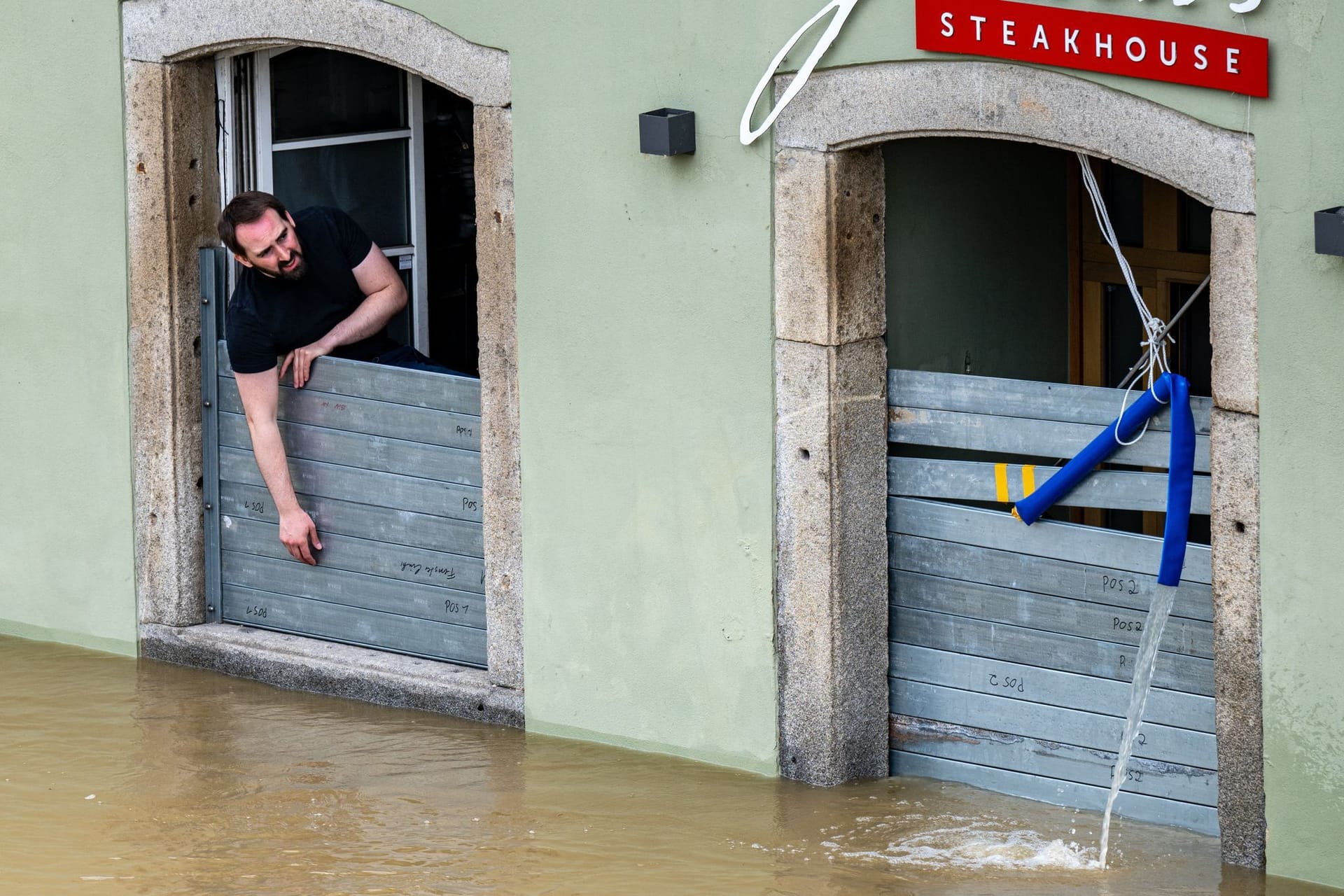 Ein Mann schaut aus einem Fenster auf das Hochwasser vor seiner Tür.