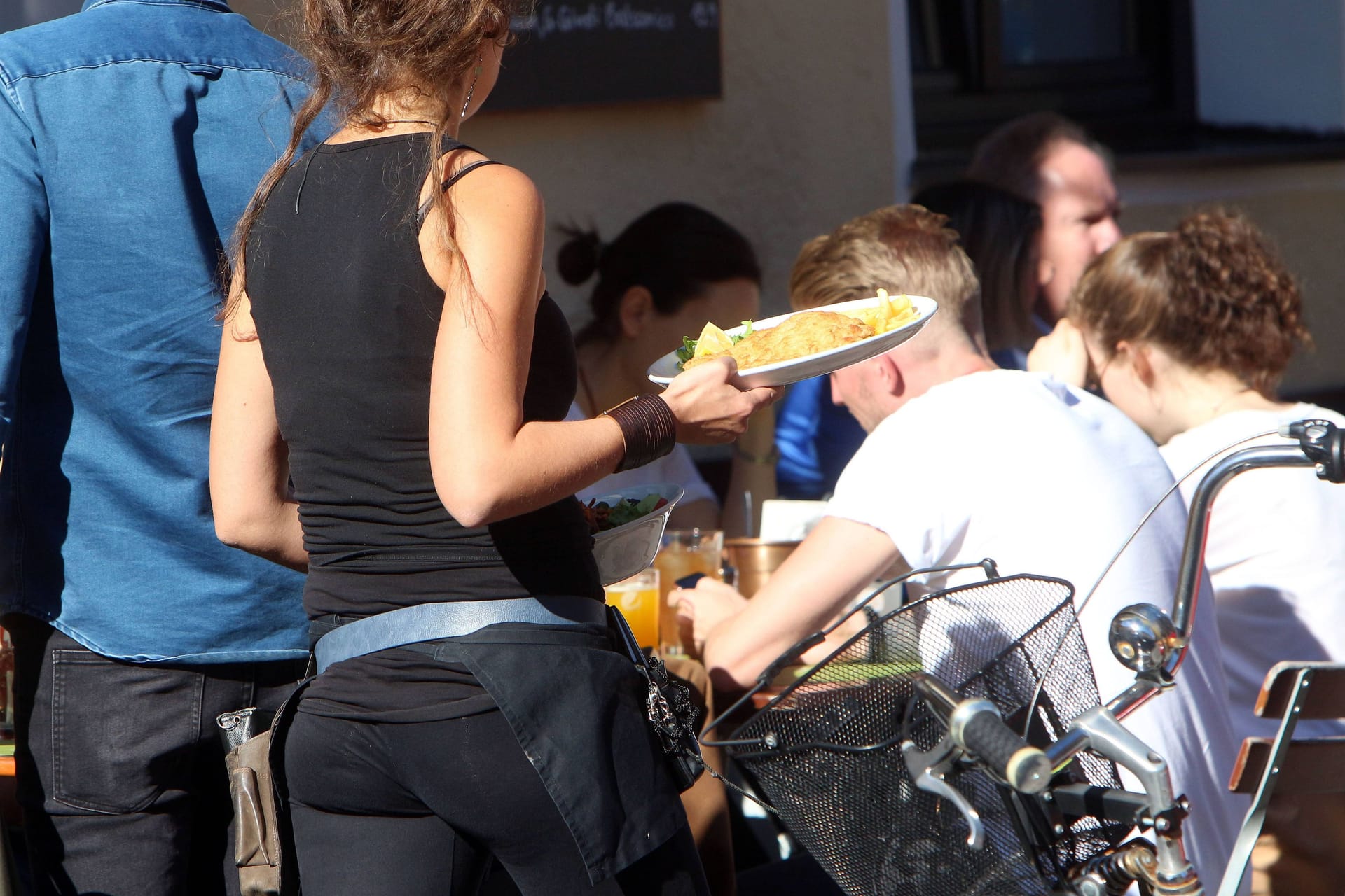 Eine Kellnerin trägt Speisen und Getränke an einem Tisch im Außenbereich eines Restaurants (Symbolfoto): Ein Restaurants in Ottensen kämpft um seine Außenterrasse.