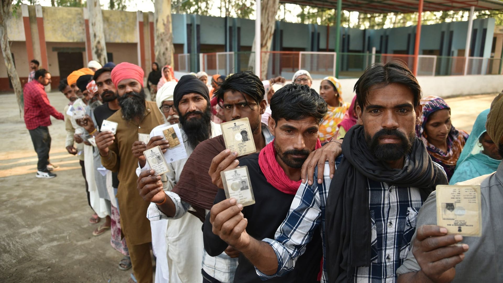 Indien, Amritsar: Menschen zeigen ihre Wahlkarten, während sie an einem heißen Sommertag während der siebten und letzten Phase der Parlamentswahl in Indien in einer Schlange stehen, um ihre Stimme abzugeben.