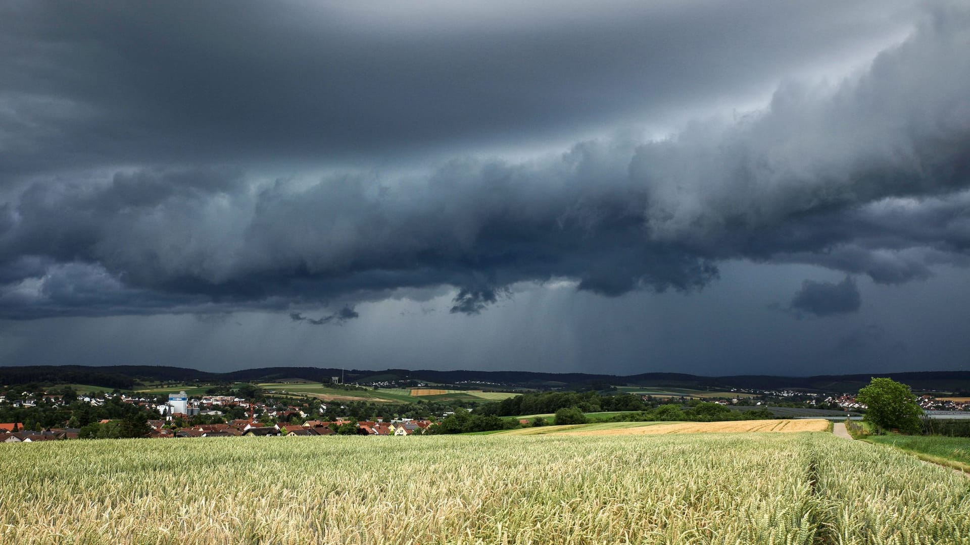 Eine Gewitterzelle mit dunklen Wolken baut sich am Himmel und hinter Feldern nahe Heilbronn auf.