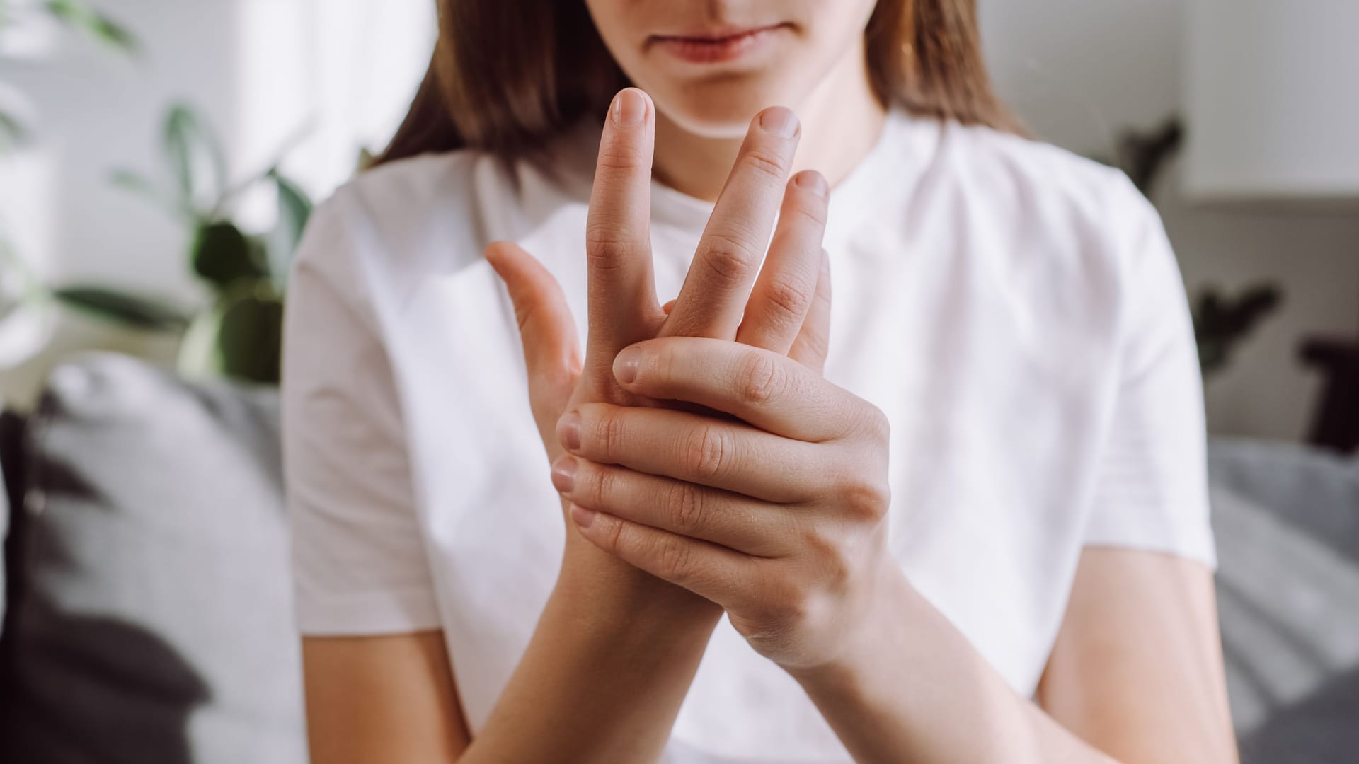 Frau mit Fingerschmerzen: Wer einen Schnappfinger entwickelt, fragt sich häufig, was diesen verursacht hat.