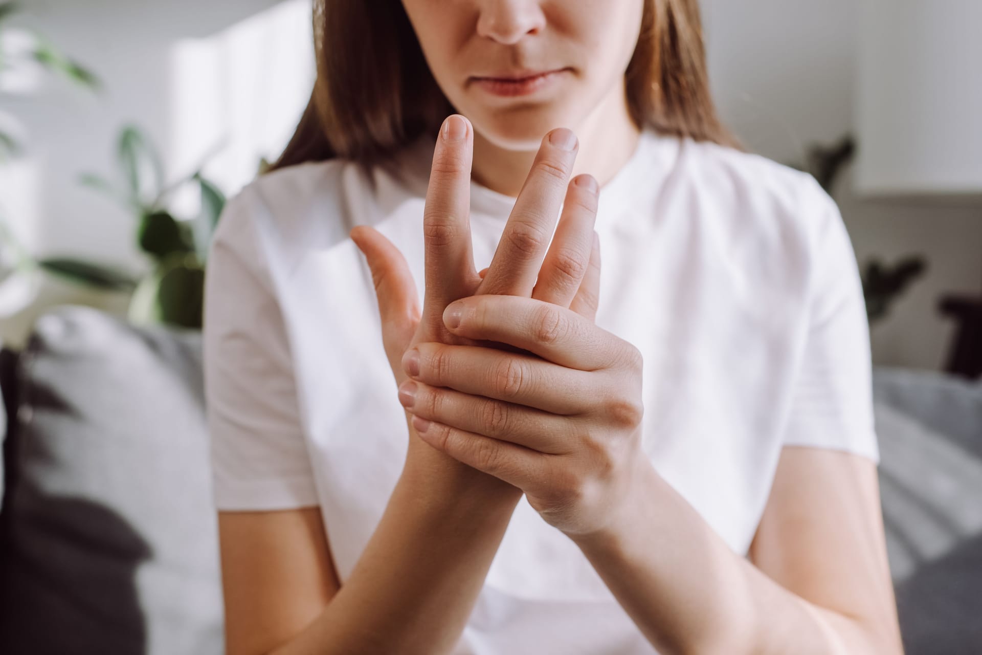 Frau mit Fingerschmerzen: Wer einen Schnappfinger entwickelt, fragt sich häufig, was diesen verursacht hat.