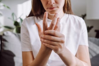 Frau mit Fingerschmerzen: Wer einen Schnappfinger entwickelt, fragt sich häufig, was diesen verursacht hat.