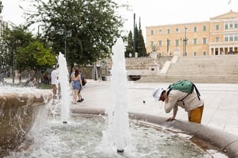 Ein Mann erfrischt sich an einem Springbrunnen auf dem Athener Syntagma-Platz.