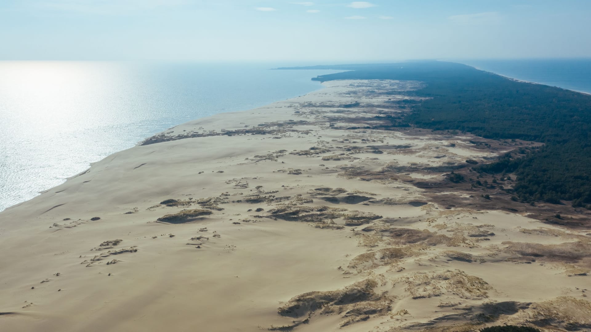 A view from a height of a narrow and long sandy saber-shaped strip of land separating the Curonian Lagoon from the Baltic Sea. Gray sand dunes of the Curonian Spit.