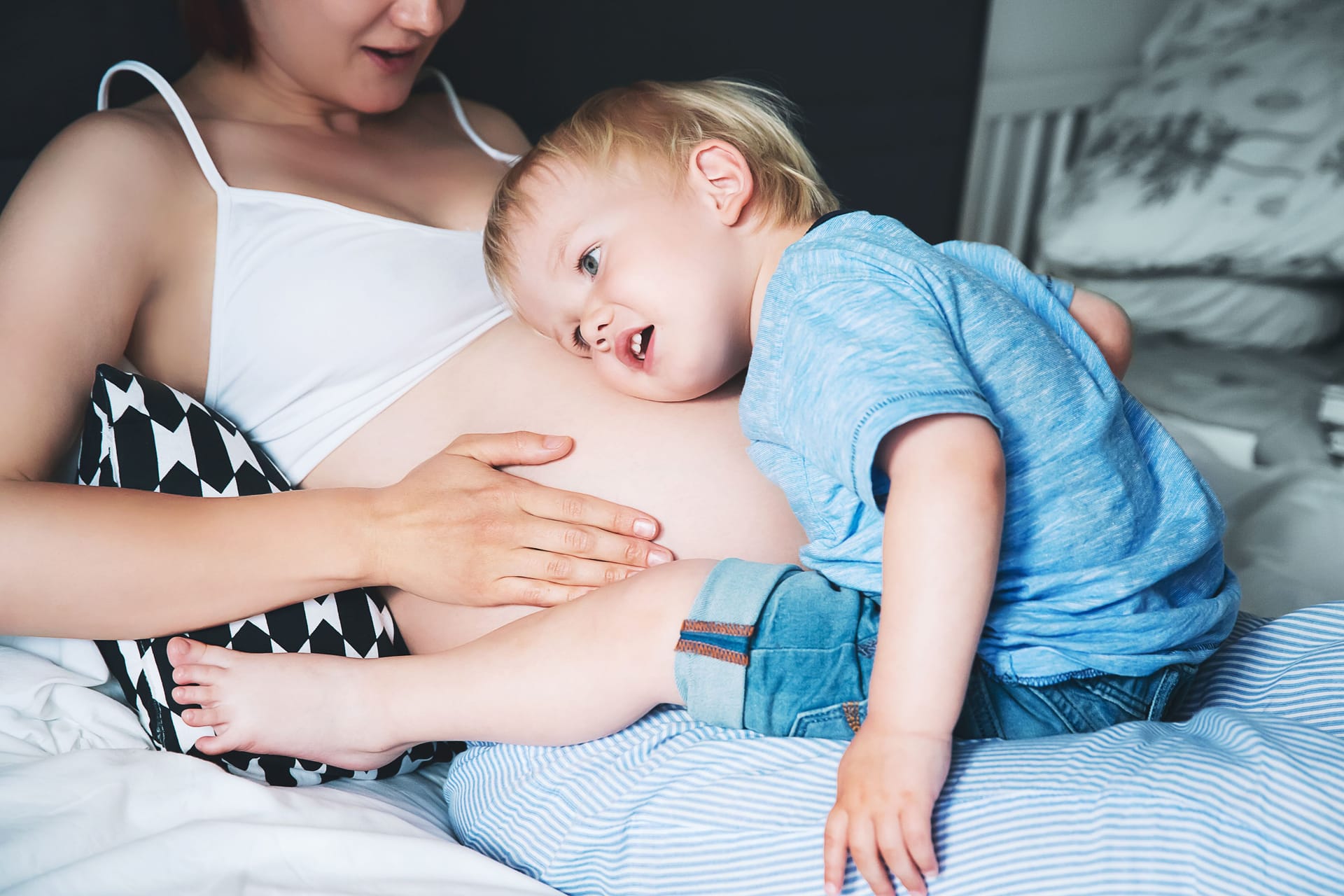 Ein Kind legt seinen Kopf auf den Bauch seiner schwangeren Mutter