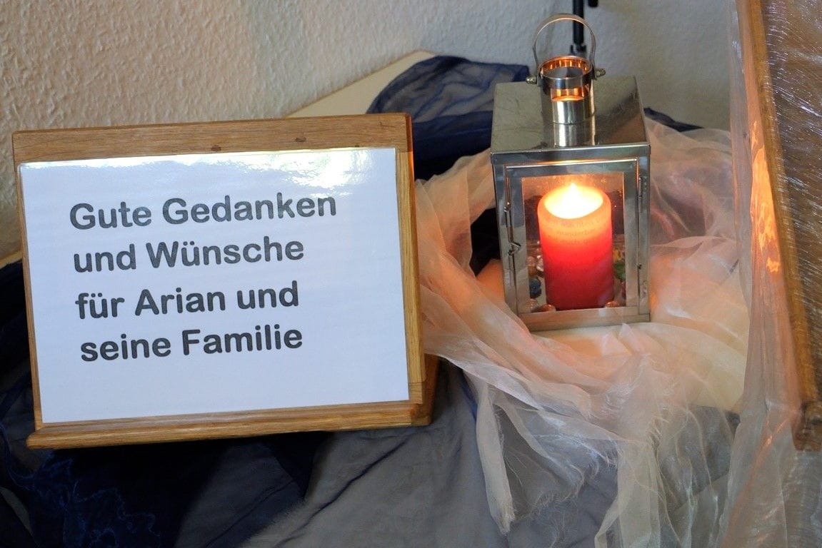 Ein Schild steht neben einer Kerze und ein Buch mit einem Regenbogen auf dem Umschlag liegt daneben: Die Kirche in Elm will Platz zum Trauern geben.