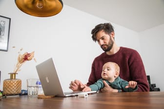 Ein Mann sitzt zusammen mit seinem Baby am Computer