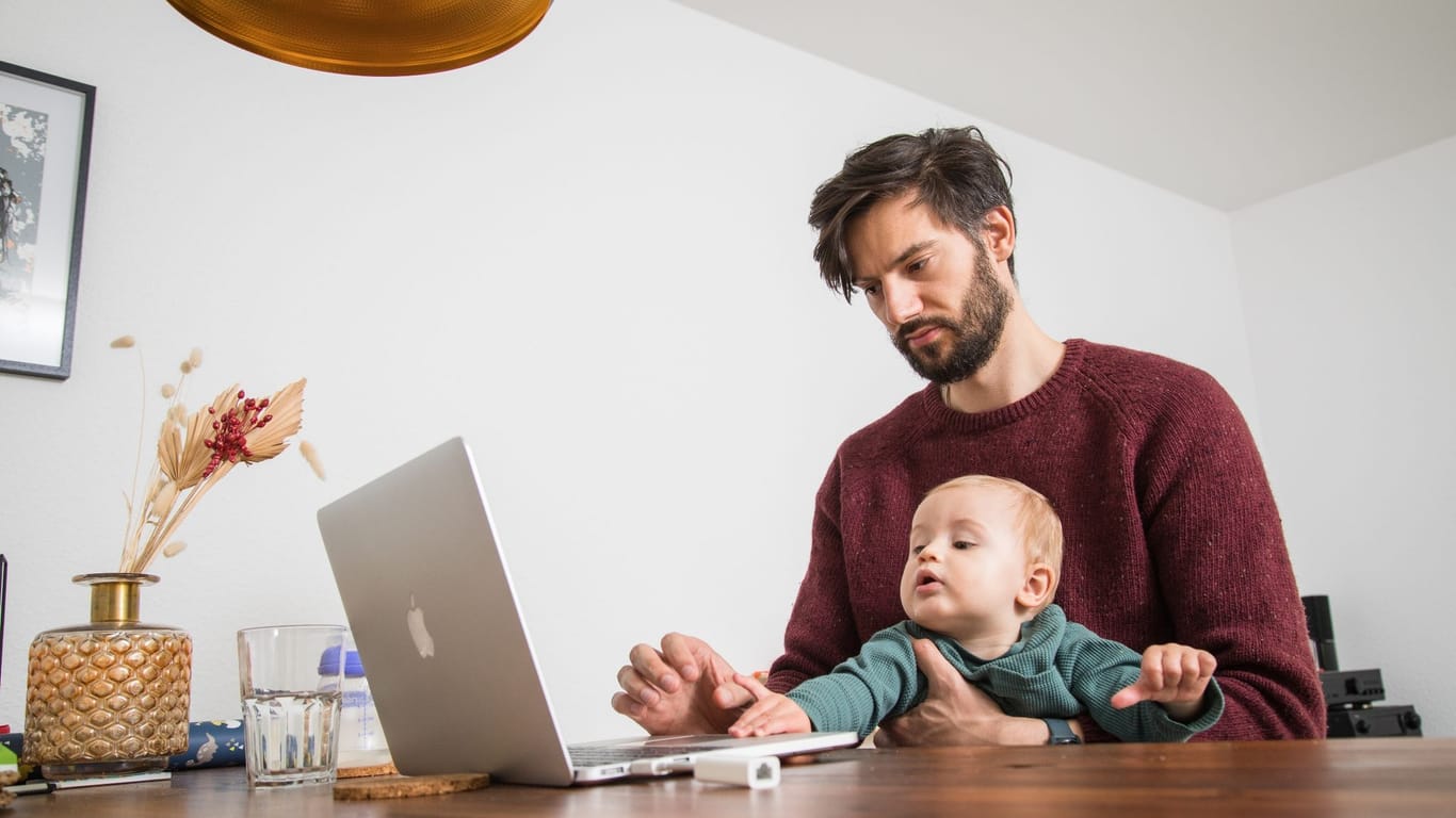 Ein Mann sitzt zusammen mit seinem Baby am Computer
