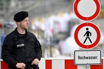 Polizist vor einem Hochwasserwarnschild (Symbolbild): Der Hochwasserschutz in Bayern hinkt seit Jahren den selbstgesteckten Zielen hinterher.