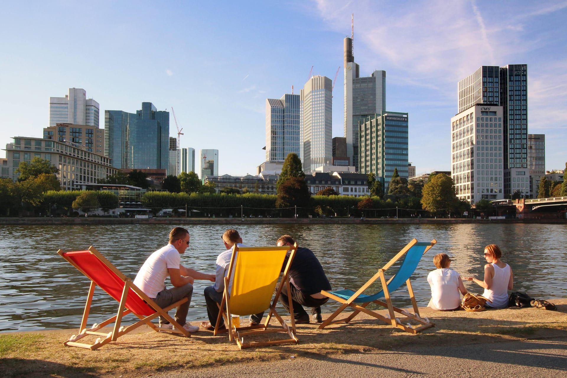 Menschen sitzen in Liegestühlen am Mainufer und genießen die Abendsonne: In den nächsten Tagen wird es in Frankfurt sommerlich-warm.