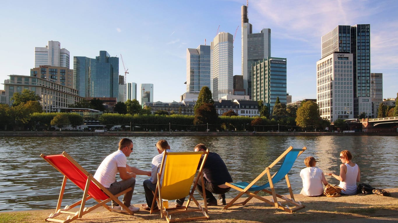 Menschen sitzen in Liegestühlen am Mainufer und genießen die Abendsonne: In den nächsten Tagen wird es in Frankfurt sommerlich-warm.