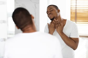 Ein Mann schaut in den Spiegel und befühlt seinen Hals