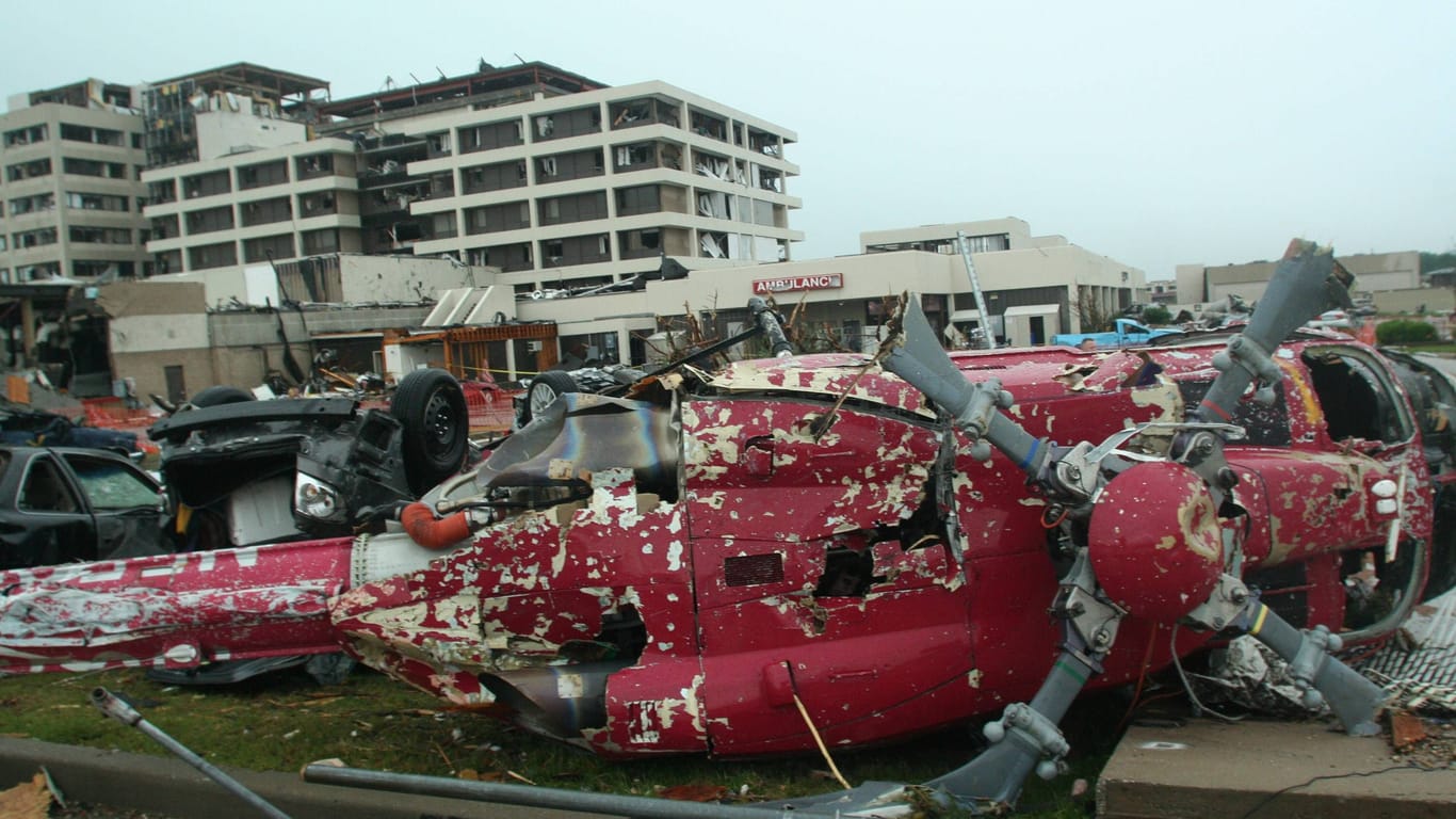 Joplin im Jahr 2011: Ein Helikopter und umher gewirbelte Autos liegen zerstört auf der Erde, im Hintergrund das schwerbeschädigte Saint Johns Hospital. Eines der Gebäude wurde aus dem Fundament gerissen und um zehn Zentimeter versetzt.