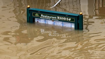 Rhodos versinkt in der Donau: Ein Schild mit der Speisekarte eines Restaurants steht im Hochwasser.