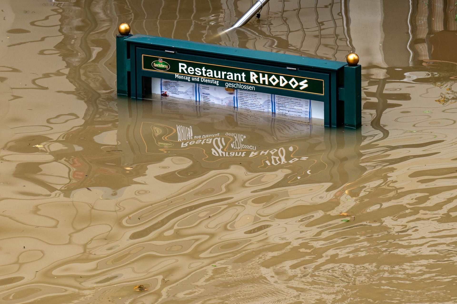 Rhodos versinkt in der Donau: Ein Schild mit der Speisekarte eines Restaurants steht im Hochwasser.