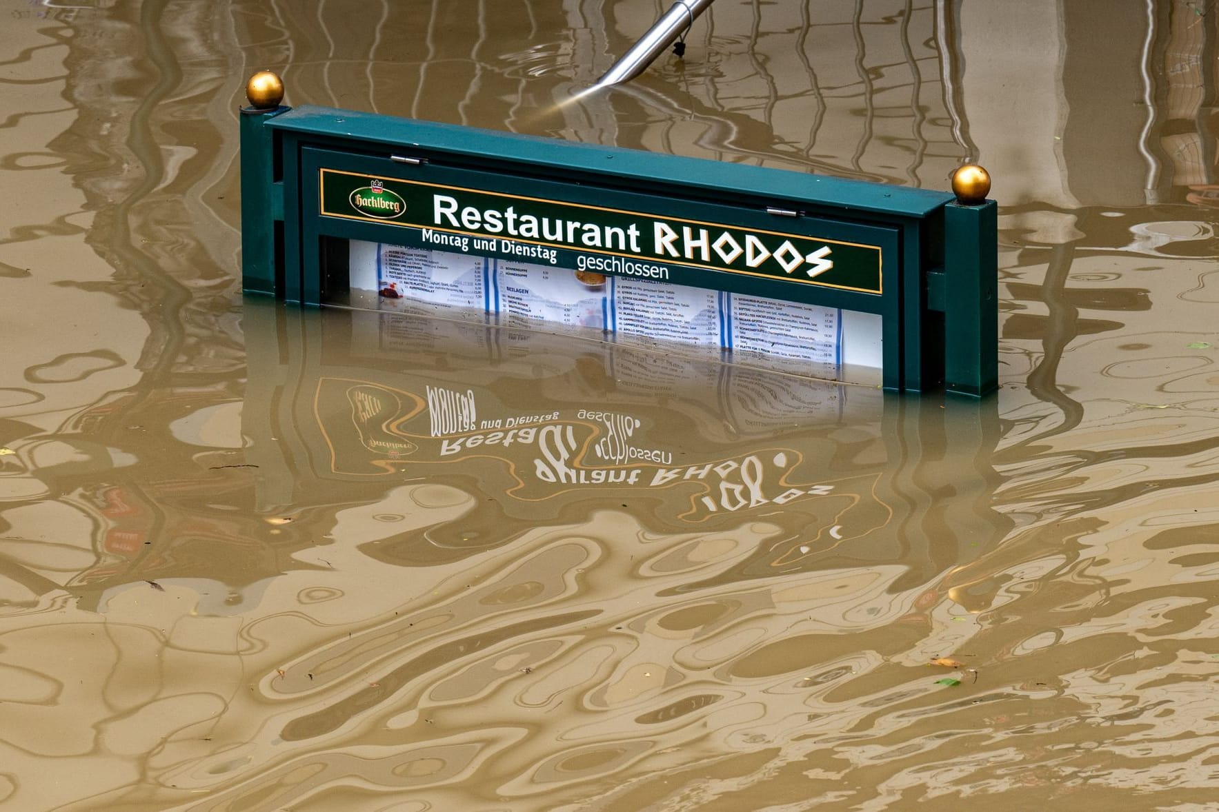 Rhodos versinkt in der Donau: Ein Schild mit der Speisekarte eines Restaurants steht im Hochwasser.