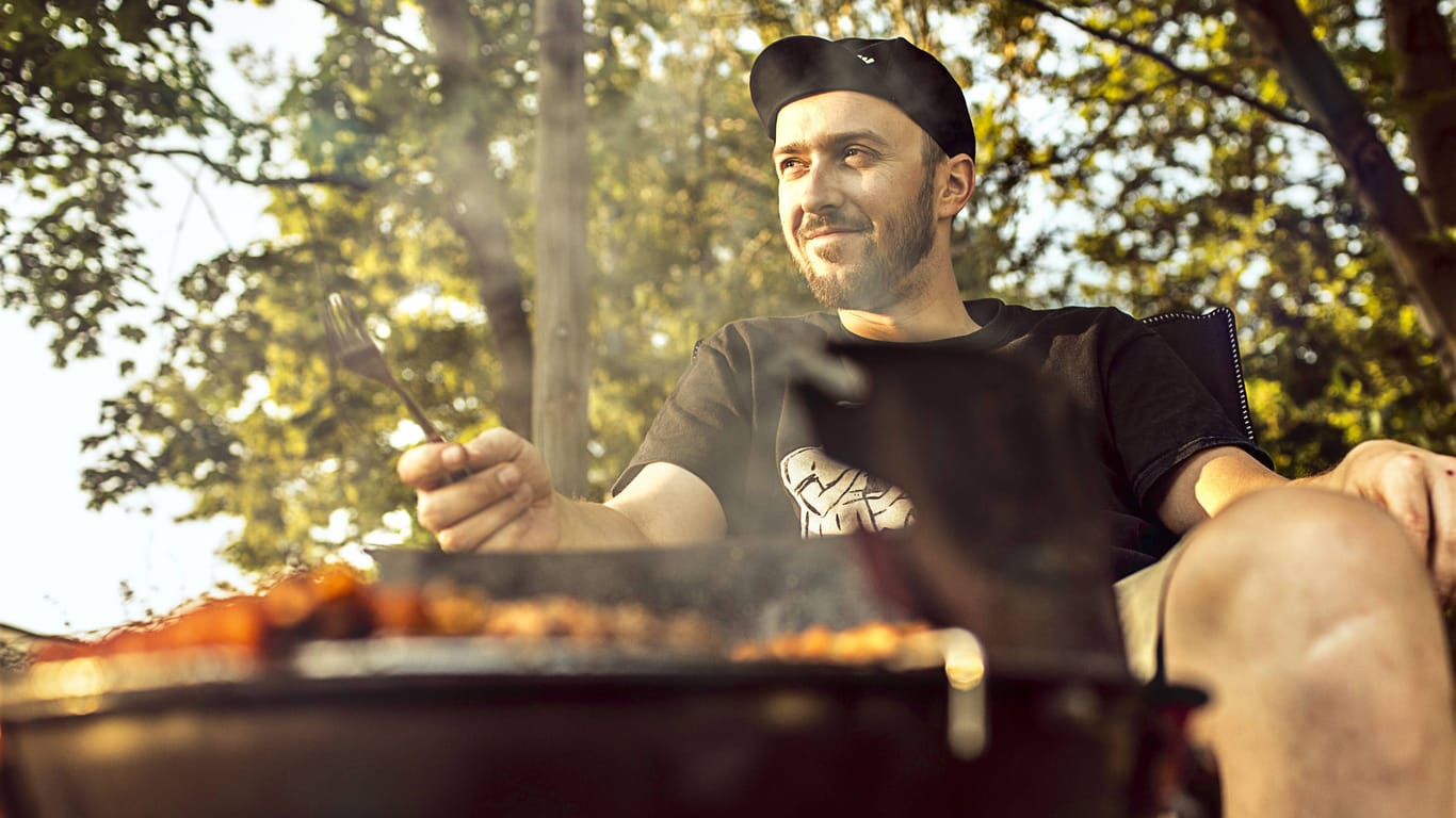 Ein Mann sitzt vor einem Grill in Hannover: Wer draußen grillen möchte, sollte sich an die Vorgaben halten.