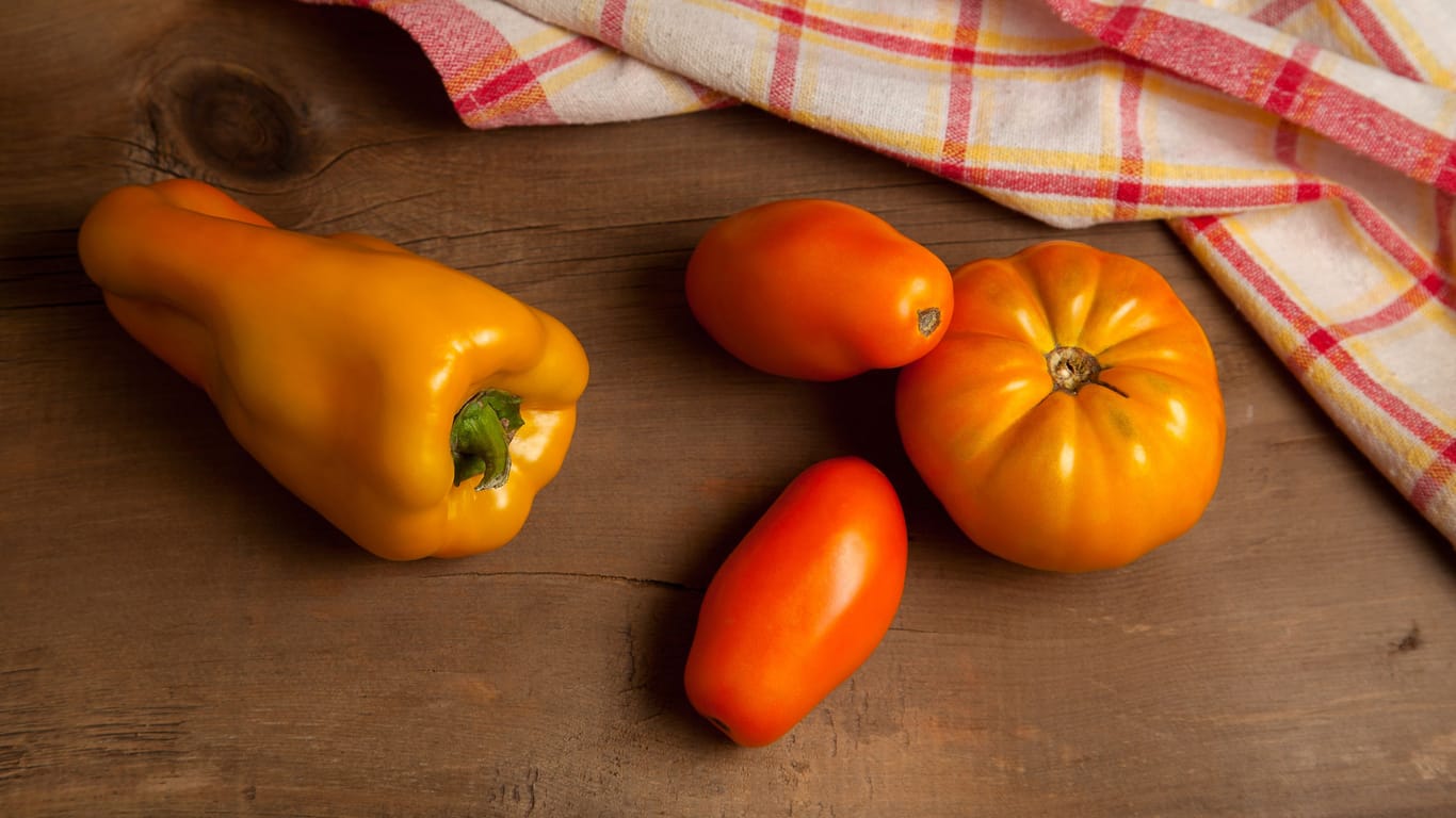 Yellow tomatoes and bell pepper on wooden background with red kitchen towel.