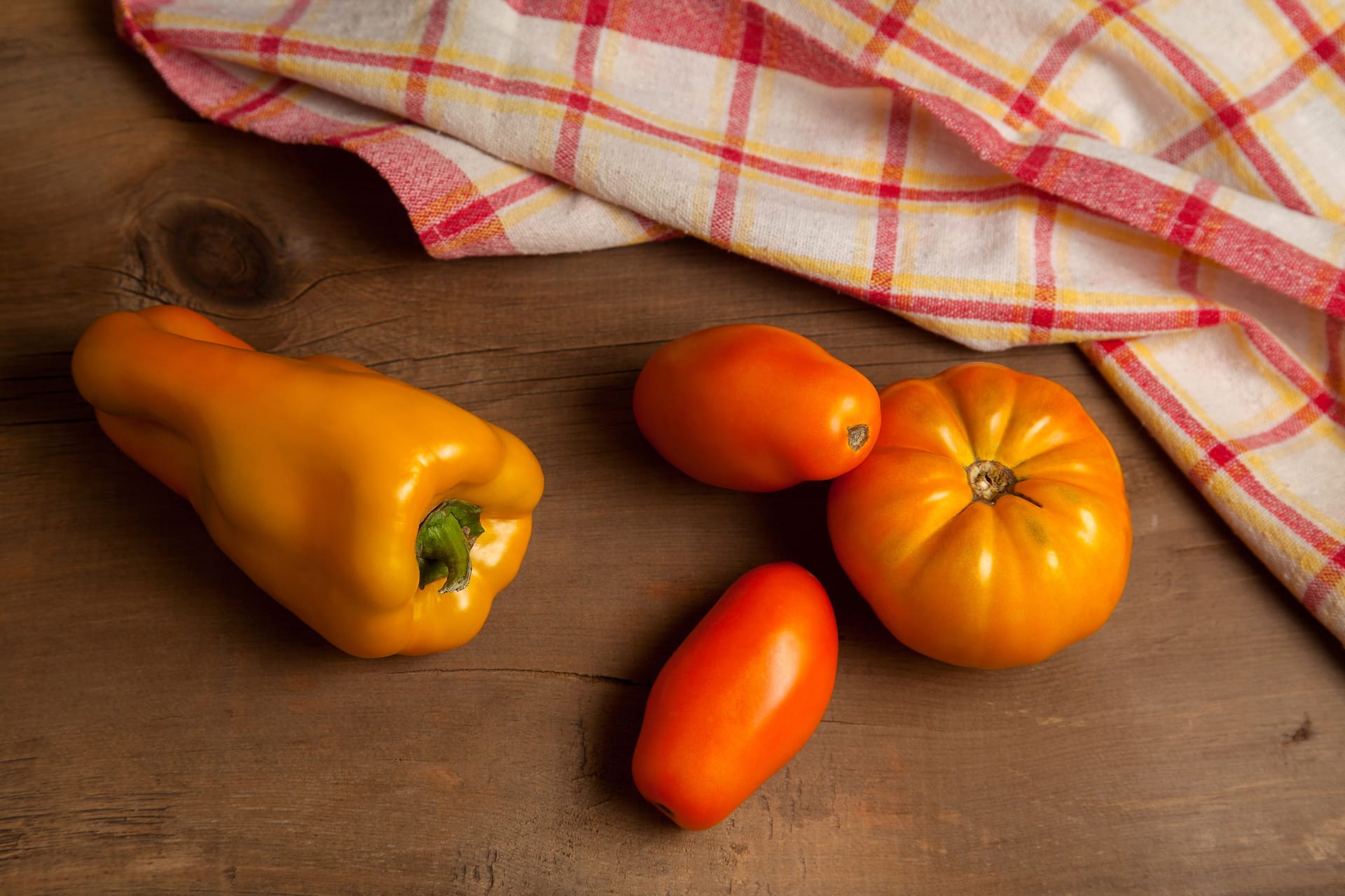 Yellow tomatoes and bell pepper on wooden background with red kitchen towel.