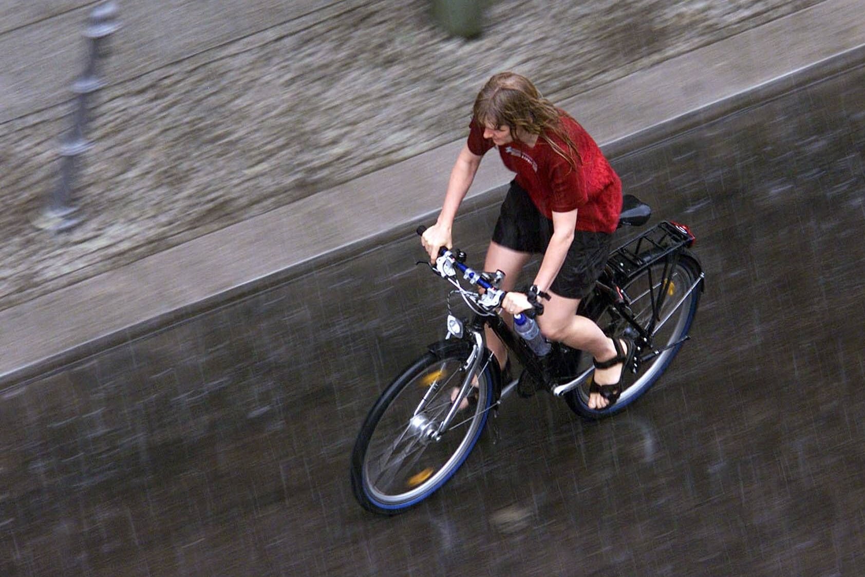 Eine Fahrradfahrerin fährt durch einen Platzregen (Archivbild): In der nächsten Woche erwarten die Wetterdienste wieder teils heftige Regenschauer.