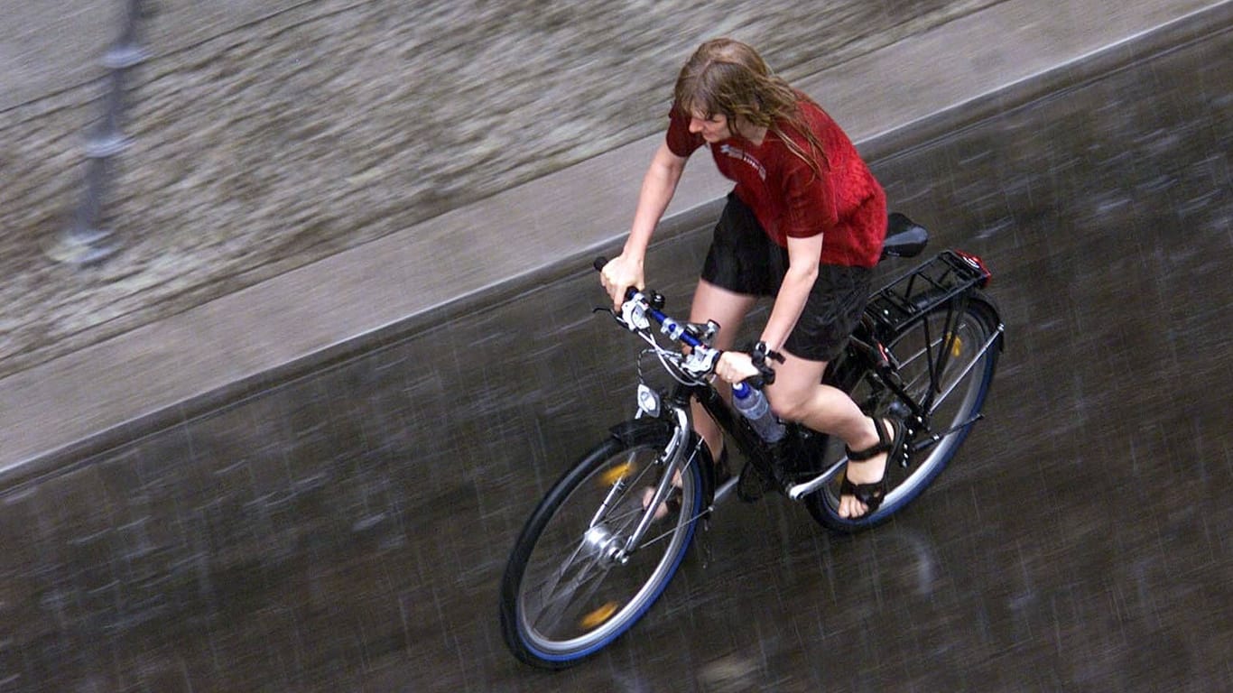 Eine Fahrradfahrerin fährt durch einen Platzregen (Archivbild): In der nächsten Woche erwarten die Wetterdienste wieder teils heftige Regenschauer.