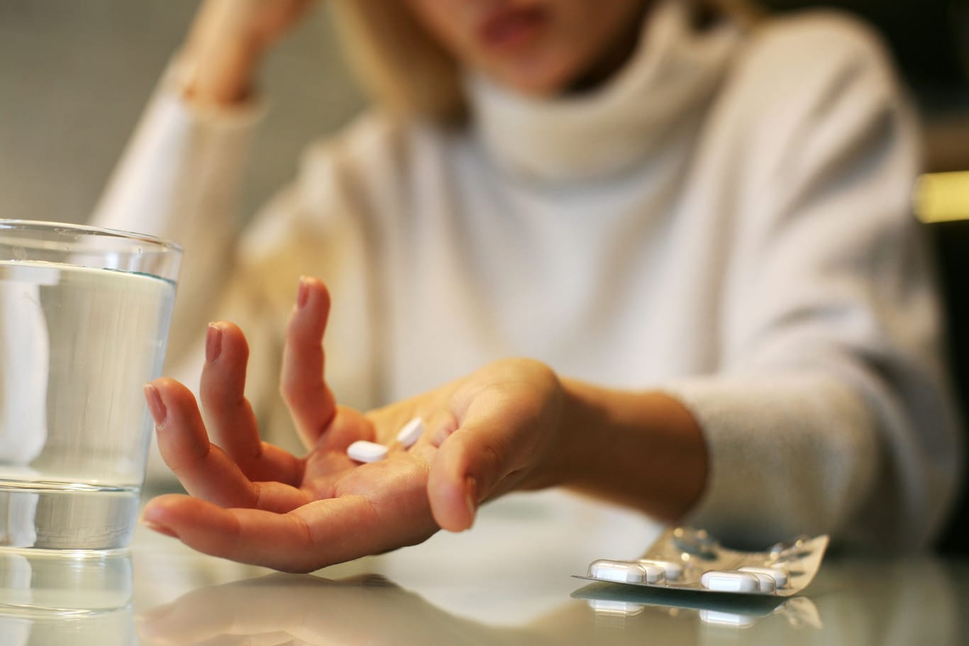 Frau hält Tabletten in der Hand, neben ihr ein Glas Wasser