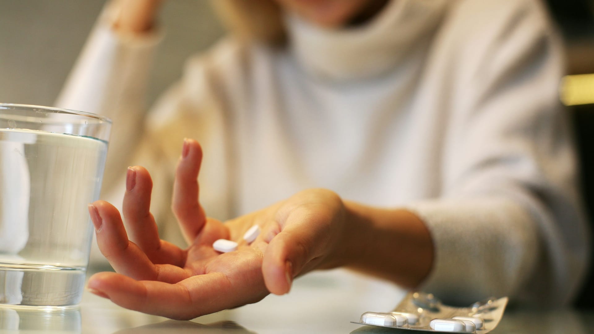 Frau hält Tabletten in der Hand, neben ihr ein Glas Wasser