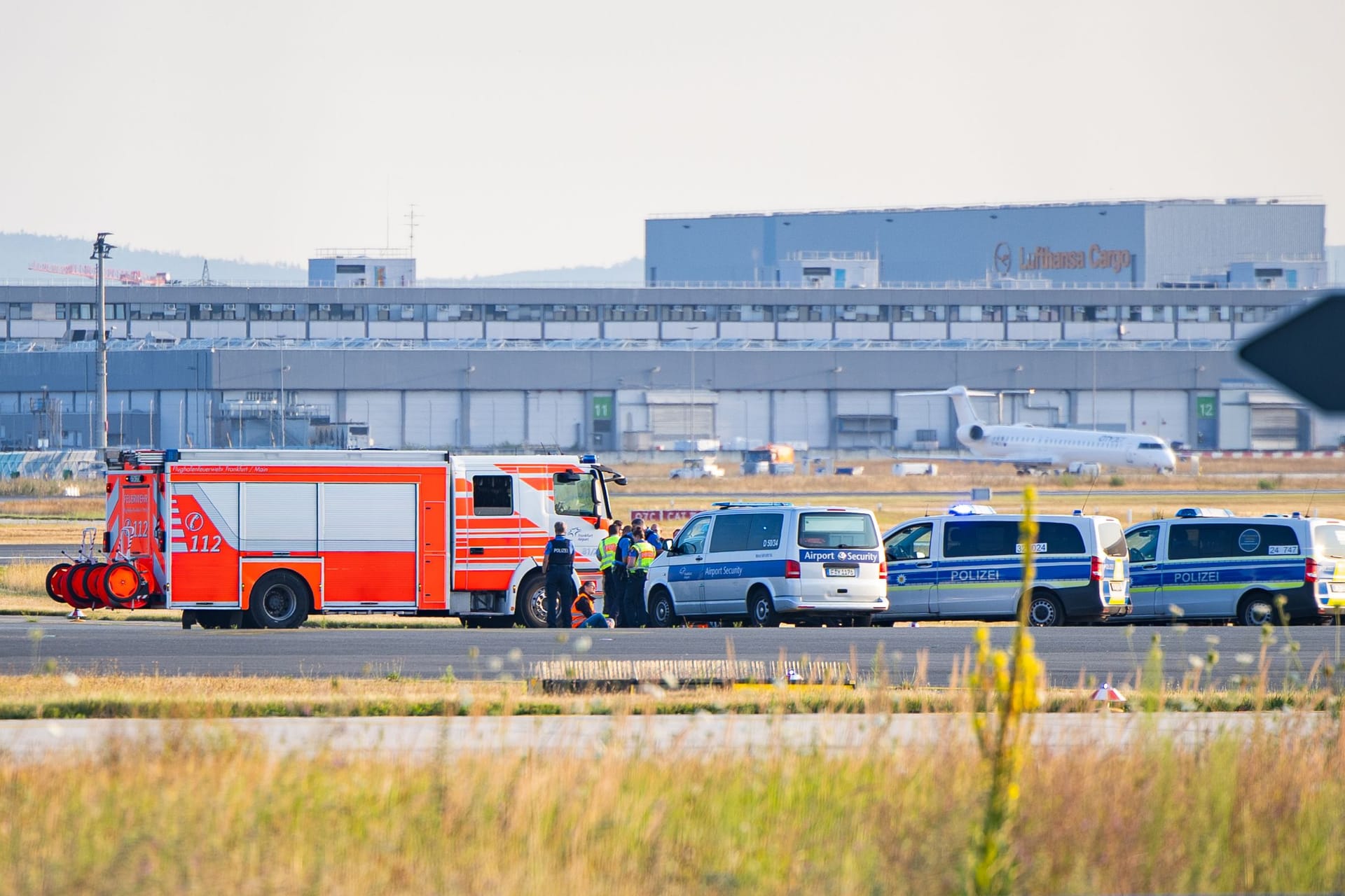 Klimakleber auf dem Rollfeld am Frankfurter Flughafen, umkreist von Polizei und Feuerwehr.