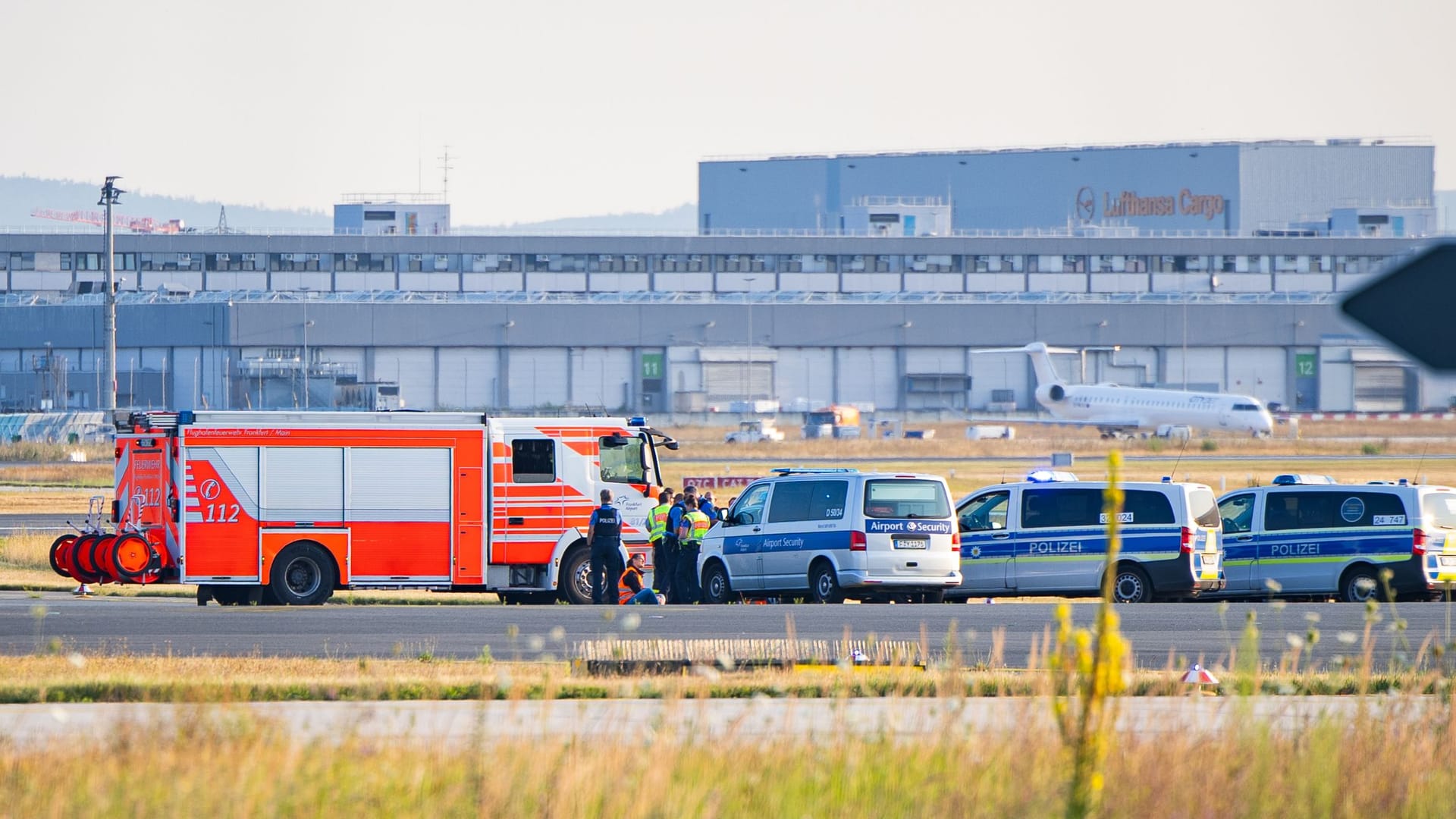 Klimakleber auf dem Rollfeld am Frankfurter Flughafen, umkreist von Polizei und Feuerwehr.