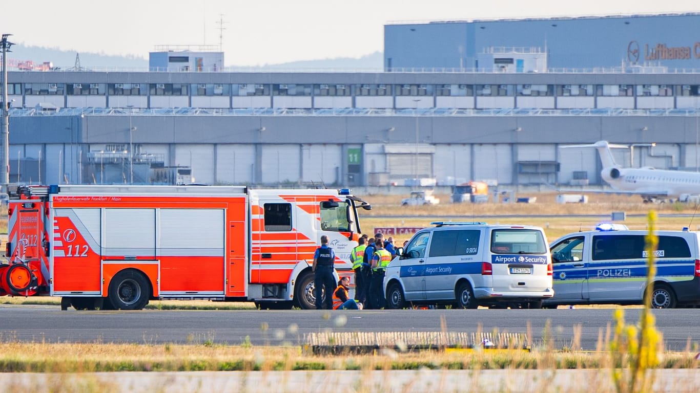 Klimakleber auf dem Rollfeld am Frankfurter Flughafen, umkreist von Polizei und Feuerwehr.