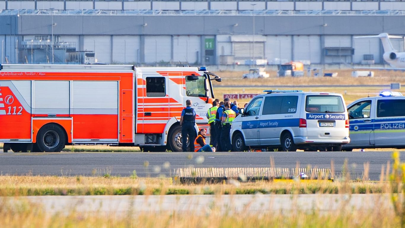 Klimakleber auf dem Rollfeld am Frankfurter Flughafen, umkreist von Polizei und Feuerwehr.