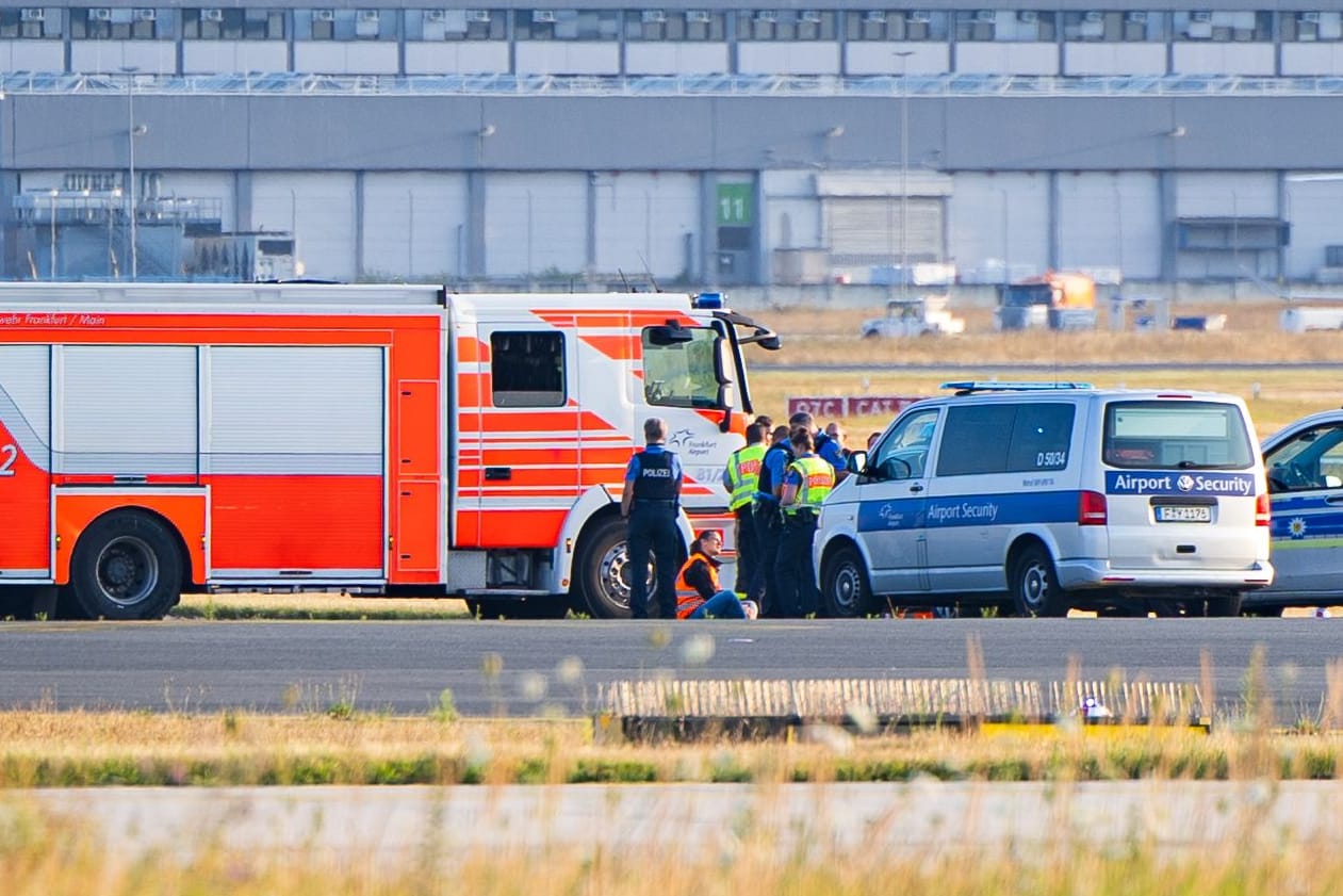 Klimakleber auf dem Rollfeld am Frankfurter Flughafen, umkreist von Polizei und Feuerwehr.