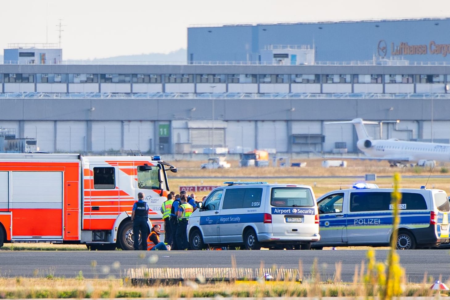 Klimakleber auf dem Rollfeld am Frankfurter Flughafen, umkreist von Polizei und Feuerwehr.