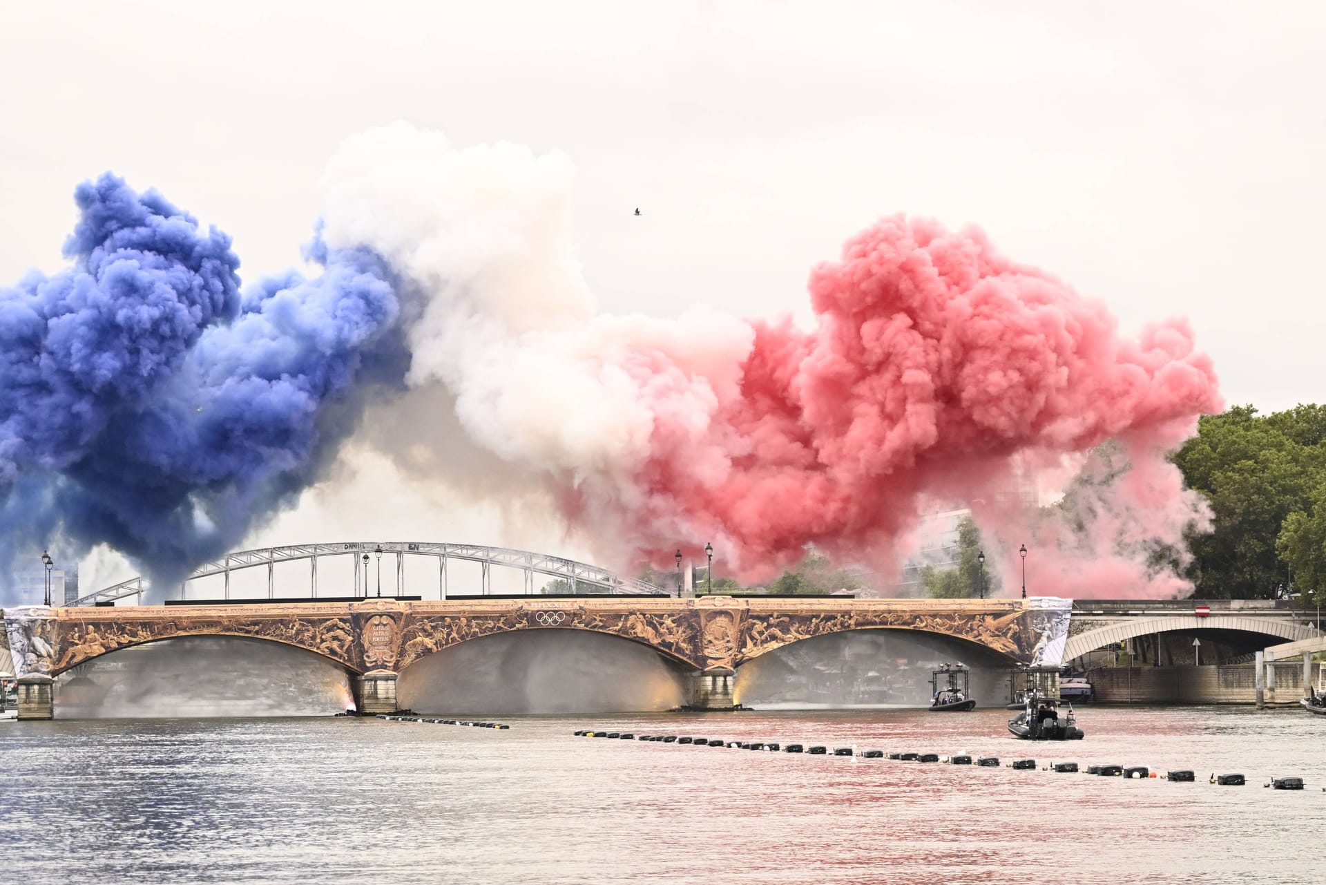 Rauchschwaden in den Farben der französischen Flagge über der Brücke Pont d’Austerlitz gaben den Startschuss zu einer sechs Kilometer langen Bootstour der Athleten entlang der Seine.