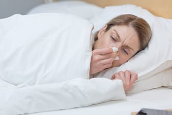 Frau liegt im Bett und hält sich ein Taschentuch an die Nase