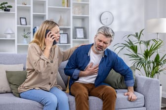 Ein Mann mit Bauchschmerzen, daneben eine Frau, die den Notdienst ruft.