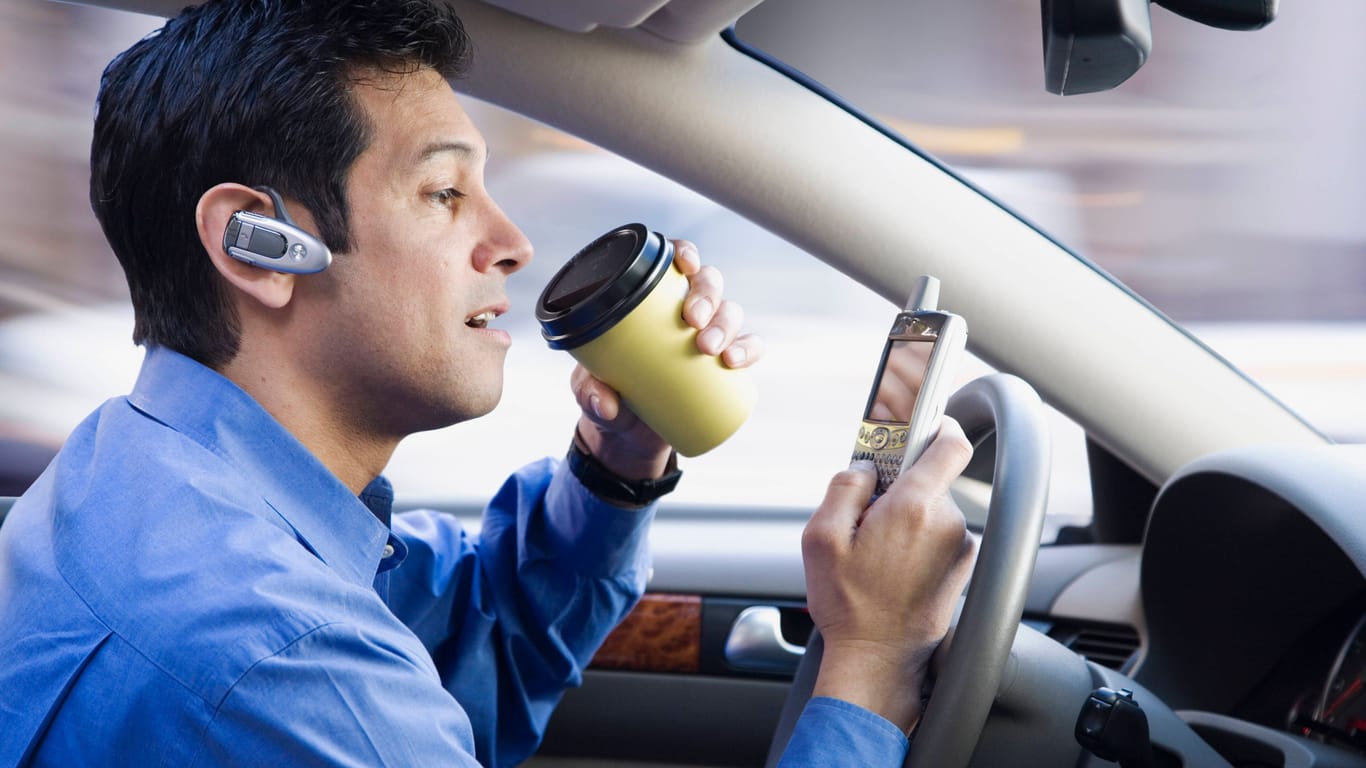 Ein Businessmann, der gleichzeitig Auto fährt, telefoniert und einen Kaffee trinkt.855