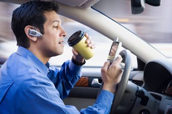Ein Businessmann, der gleichzeitig Auto fährt, telefoniert und einen Kaffee trinkt.855